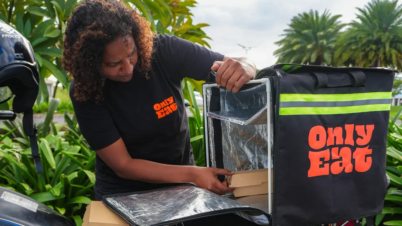 An OnlyEat rider loading takeaway boxes into the insulated bag for an evening food delivery in Mauritius.